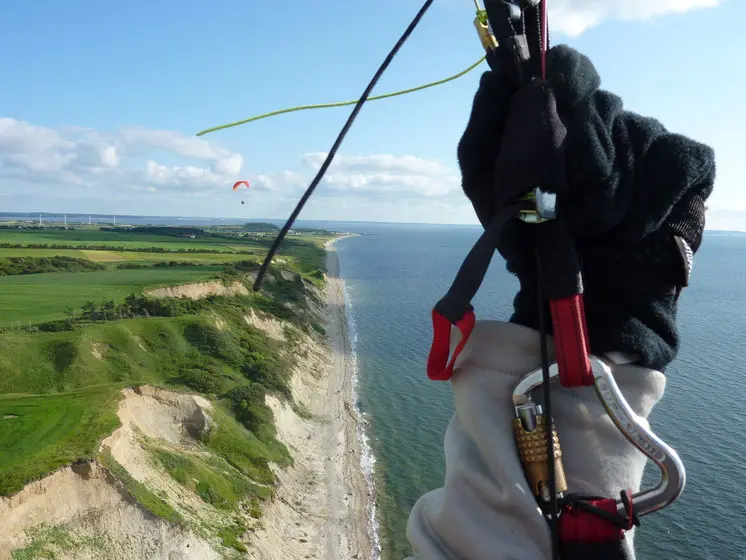 Blick aus der Perspektive eines Gleitschirmfliegers auf die Küste Dänemarks mit grünen Feldern und blauem Meer unter klarem