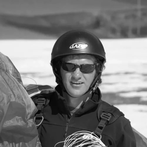 Mann mit Helm und Sonnenbrille hält Gleitschirm und Leinen in der Hand, Outdoor-Szenerie bei Austriafly Flugschule